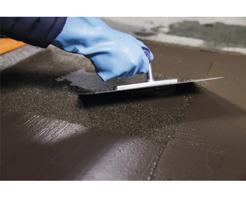 Hand mit Handschuh glättet Estrich mit einer Glättkelle