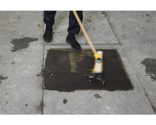 Eine Person reinigt mit einer Bürste eine Steinterrasse.