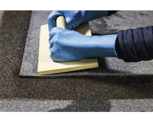 Verlegen von Teppichfliesen mit Glättkelle durch eine Person mit Handschuhen