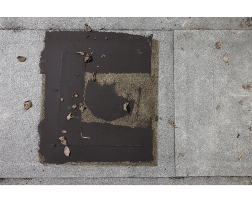 Graue Terrassenplatten mit abgenutzter, dunkler Imprägnierung und Laub