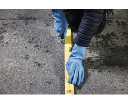 Handwerker schneidet Dachpappe mit einem Cuttermesser entlang einer Wasserwaage.