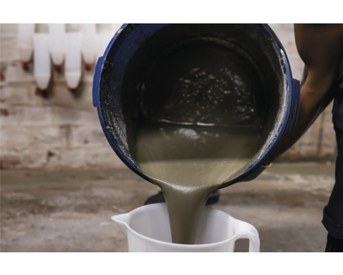 Fließestrich wird aus einem Eimer in einen Messbecher gegossen.