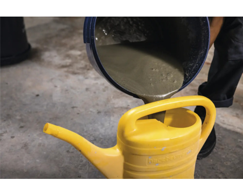 Aus einem Eimer wird Beton in eine gelbe Gießkanne gegossen.