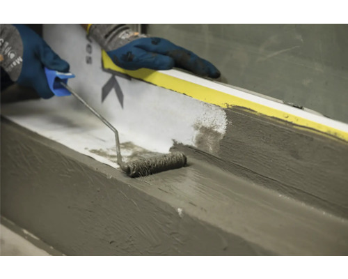 Auftragen einer Dichtungsmasse mit einer Rolle auf einer Fensterbank.