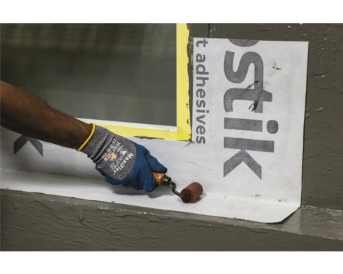 Eine Person verwendet eine Rolle, um Dichtungsbahnen an einem Fenster anzubringen.