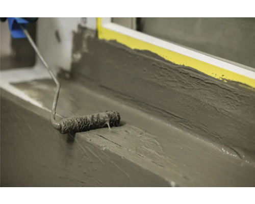 Auftragen von Dichtmasse mit einer Farbwalze auf einer Fensterbank.