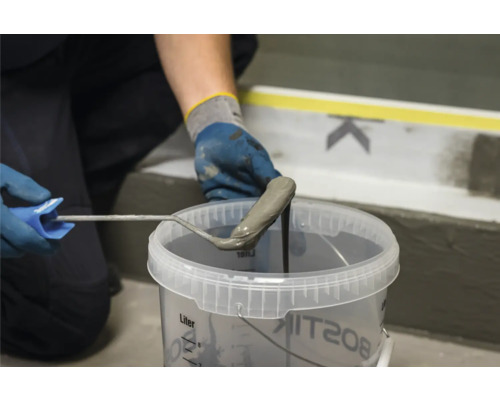 Hand mit Farbroller taucht in einen Eimer mit Dichtmasse von Bostik