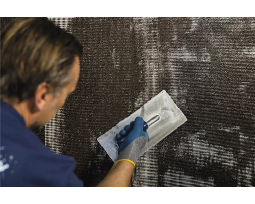 Mann trägt Armierungsmörtel mit einer Glättkelle auf ein Gewebe auf.