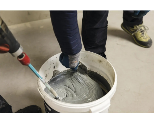 Handwerker mischt Fliesenkleber im Eimer mit Rührgerät und Spachtel