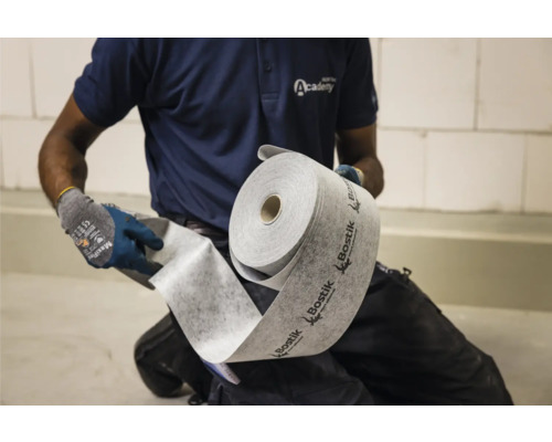 Eine Person rollt eine Rolle Bostik-Dämmunterlage aus