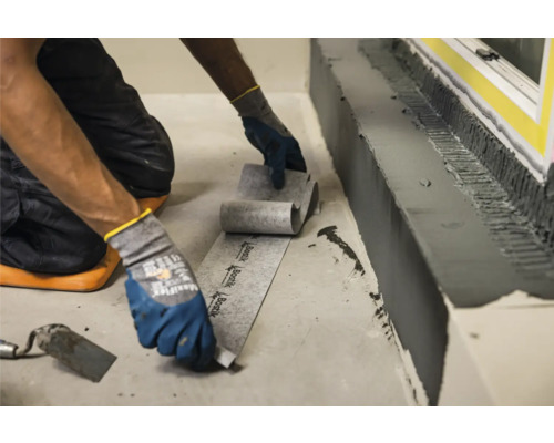 Eine Person verlegt Dichtband zur Abdichtung im Innenbereich.