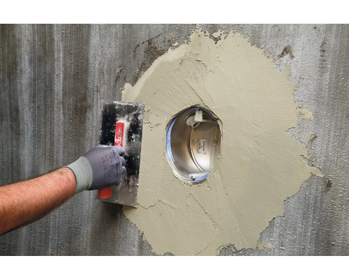 Handwerker trägt Spachtelmasse auf eine Wand auf, um eine Aussparung zu füllen.