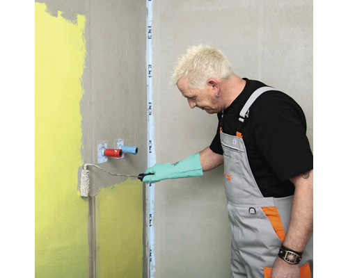 Handwerker trägt Dichtschlämme mit einer Farbwalze auf die Wand im Badezimmer auf.