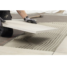 Fliesenleger bei der Arbeit: Verlegen von Fliesen mit Fliesenkleber.