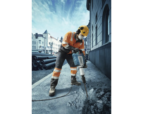 Ein Bauarbeiter mit Schutzkleidung benutzt einen Abbruchhammer, um Beton aufzubrechen.