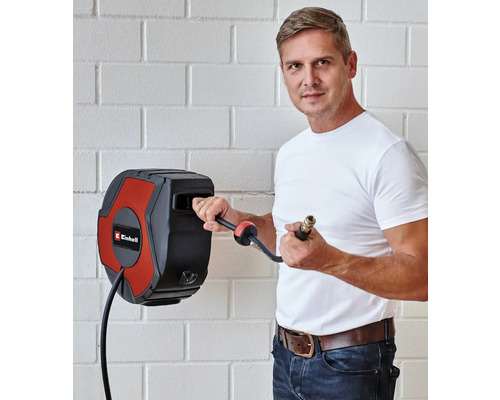 Ein Mann benutzt eine automatische Schlauchtrommel der Marke Einhell an einer Wand.