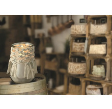 Dekorative Kerze im Glas mit Makramee-Verzierung auf Holzfass