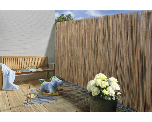 Szene mit Bambusmattenzaun, Holzbank und Gartendekoration auf einer Holzterrasse
