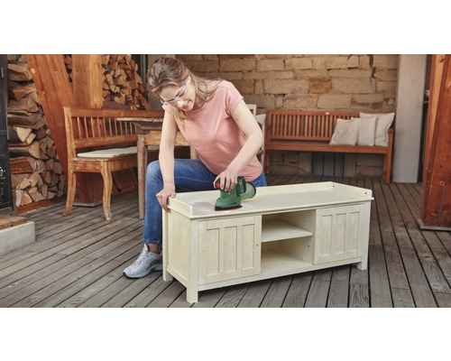 Frau schleift Holzkommode mit einem Exzenterschleifer im Außenbereich.