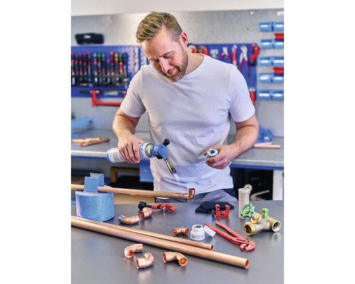 Mann lötet Kupferrohre mit einem Gasbrenner, umgeben von Kupferrohrverbindungsstücken und Werkzeugen