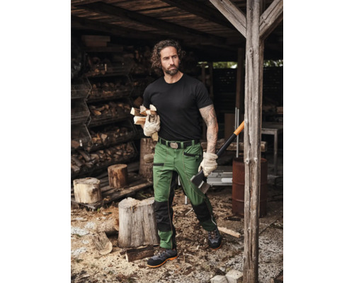 Mann in Arbeitskleidung mit Axt und Holz vor Holzschuppen