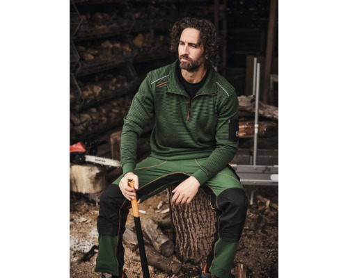 Mann in Forstbekleidung mit Axt vor Holzstapel