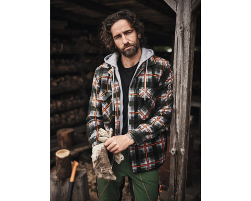 Mann mit Holzfällerhemd, Arbeitshose und Handschuhen vor Holzhütte