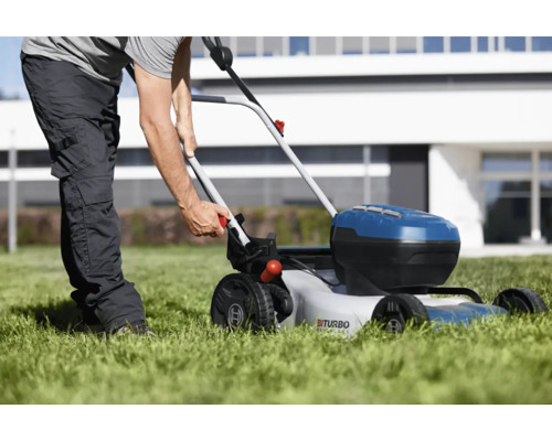 Eine Person benutzt einen Akku-Rasenmäher auf einer Rasenfläche vor einem Haus.