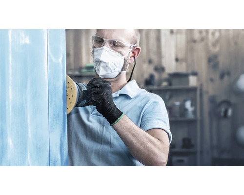 Mann schleift Holz mit Schleifgerät, Schutzbrille und Atemschutzmaske