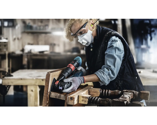 Frau schleift einen Stuhl mit einem Elektrowerkzeug in einer Werkstatt