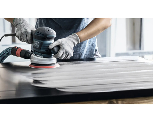 Eine Person schleift mit einem Exzenterschleifer eine Holzoberfläche.