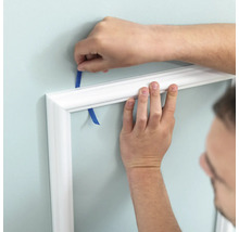 Anbringen einer weißen Zierleiste mit Klebeband an einer Wand.