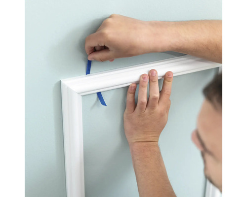 Anbringen einer weißen Zierleiste mit Klebeband an einer Wand.