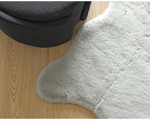 Detailansicht eines grauen Teppichs mit Schaffelloptik neben einem Sessel auf Holzboden