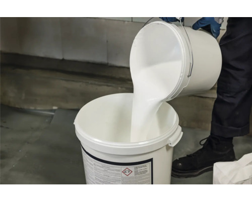 Person gießt weiße Farbe in Eimer