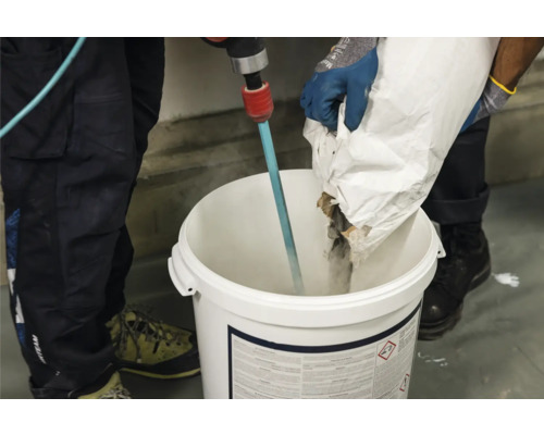 Handwerker mischt Estrichmörtel mit einem Rührwerk in einem Eimer