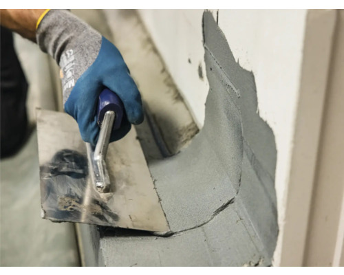 Maurerhand mit Kelle beim Auftragen von Mörtel