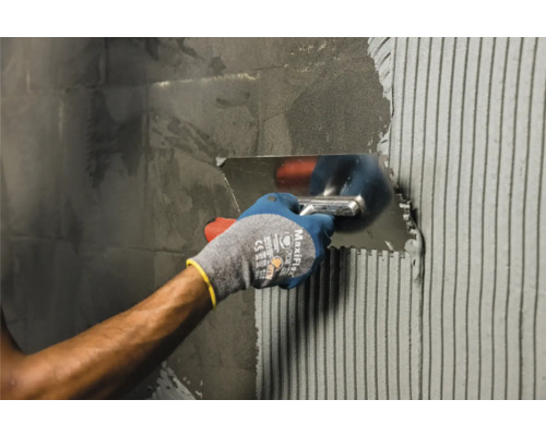 Fliesenleger trägt mit einer rostfreien Glättkelle Klebstoff auf Fliesen auf