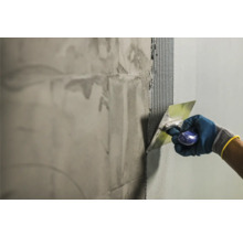 Handwerker trägt Fliesenkleber mit einer Glättkelle auf eine Wand auf.