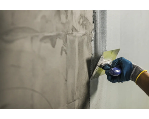Handwerker trägt Fliesenkleber mit einer Glättkelle auf eine Wand auf.