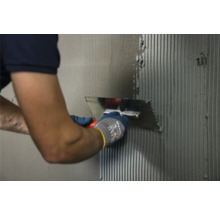 Eine Person trägt mit einer Spachtel Klebstoff auf eine Wand auf.