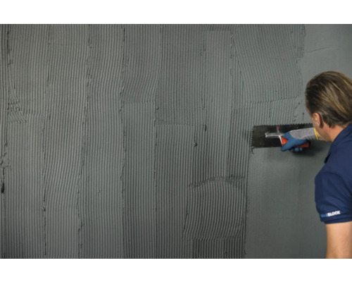 Verarbeiten von Fliesenkleber mit einer Glättkelle auf einer Wand.