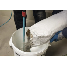 Eine Person gießt Material aus einem Sack in einen Eimer mit einem Rührwerk.