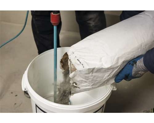 Eine Person gießt Material aus einem Sack in einen Eimer mit einem Rührwerk.