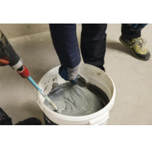 Fliesenkleber wird in einem Eimer mit einem Rührwerk und einer Spachtel gemischt.