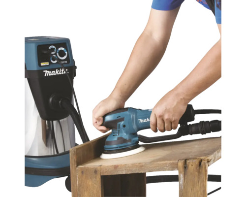 Eine Person schleift ein Holzstück mit einem Makita Exzenterschleifer und einem Staubsauger.