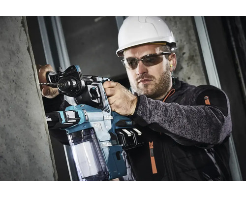 Ein Mann mit Schutzhelm und Schutzbrille bohrt mit einem Bohrhammer in eine Wand.