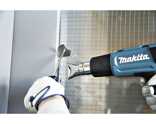 Anwendung einer Makita Heißluftpistole auf eine Oberfläche mit einem Werkzeug in der Hand.