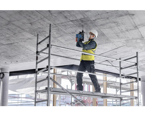 Handwerker auf einem Gerüst bohrt mit einem Bohrhammer in die Decke
