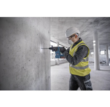 Ein Bauarbeiter bohrt mit einem Bohrhammer ein Loch in eine Betonwand.